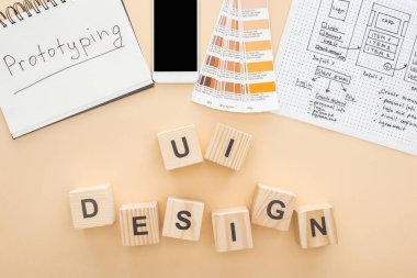 Web sitesi tasarım şablonu, renk paleti ve not defteri yakınlarındaki akıllı telefonun üst görünümü üzerinde bej arkaplan üzerinde ui tasarımı harfi olan tahta blokların üzerinde prototip yazılıdır.