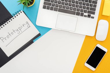 Prototip harfleri, dizüstü bilgisayarı, faresi, akıllı telefonu, soyut geometrik arkaplanı olan bitkinin üst görünümü