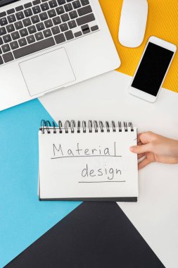Soyut geometrik arka planda dizüstü bilgisayar, akıllı telefon, bilgisayar faresi gibi materyal tasarımı harf içeren bir defter tutan bir kadın görüntüsü.