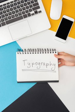 Dizüstü bilgisayar, akıllı telefon, bilgisayar faresi ve soyut geometrik arka planda tipografi harfi olan bir not defteri tutan kadının kırpılmış görüntüsü