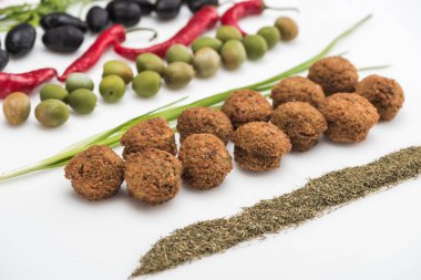 Beyaz arkaplanda zeytin, kırmızı biber, yeşil soğan, bitki ve falafel manzarası.