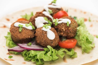 Pide üzerine taze falafel topları, sebzeler ve beyaz arka planda sos.