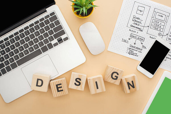 top view of gadgets near wooden blocks with design lettering, website design template and green plant on beige background