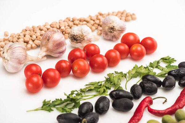 close up view of chickpea, garlic, cherry tomatoes, parsley, chili pepper, olives on white background