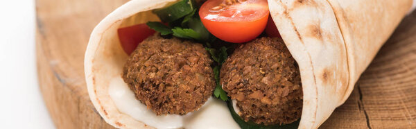 close up view of fresh falafel balls in pita with vegetables and sauce on wooden board on white background, panoramic shot