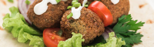 close up view of fresh falafel balls on pita with vegetables and sauce, panoramic shot