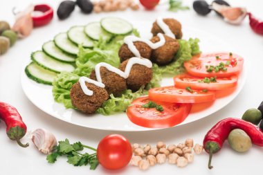 Sebzelerin seçici odağı yuvarlak çerçevede, falafel etrafına yerleştirilmiş ve sosu beyaz arkaplanda tabakta.