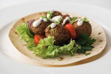 Pide soslu falafel ve beyaz tabakta sebze.