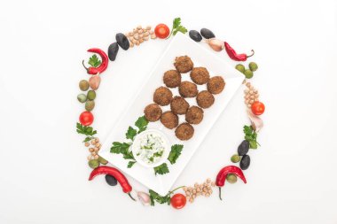 Yuvarlak çerçeveli sebze manzarası beyaz arkaplanda soslu falafel tabağın etrafına dizilmiş.