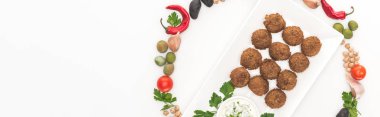Yuvarlak çerçeveli sebzelerin beyaz arka planda soslu falafel tabağın etrafına yerleştirilmiş üst görünümü, panoramik çekim