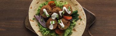 top view of falafel with vegetables and sauce on pita on wooden table, panoramic shot clipart