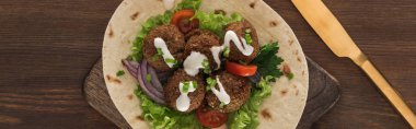 top view of falafel with vegetables and sauce on pita near knife on wooden table, panoramic shot clipart