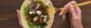 Sebzeli ve soslu falafel yiyen kadın manzarası ahşap masa çatallı, panoramik çekim