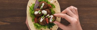 Sebzeli falafel yiyen kadın manzarası ve ahşap masada pide sosu, panoramik çekim.