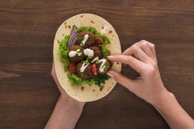 Sebzeli falafel yiyen kadın manzarası ve ahşap masada pide sosu.