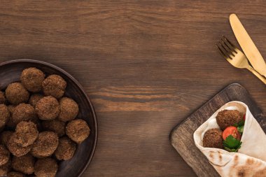 Sebzeli falafel ve soslu falafel topu ve ahşap masadaki çatal bıçak takımının yanında.