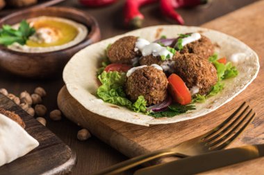 Pide üzerine falafel, ahşap masada humus yanında sebze ve sos.