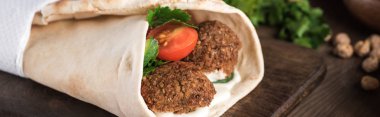 close up view of falafel with vegetables and sauce wrapped in pita on wooden table, panoramic shot clipart