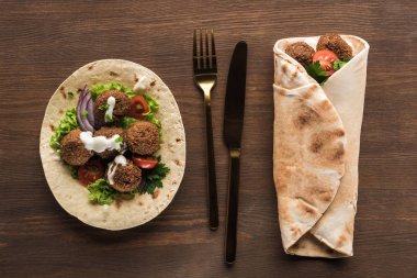 Sebze ve sosla kaplı falafel 'in en üst görüntüsü ahşap masada, çatal bıçakla paketlenmiş ve açılmıştı.