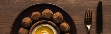 Tahta masadaki çatal bıçak takımının yanında humus kaplı falafel toplarının üst görüntüsü, panoramik çekim.