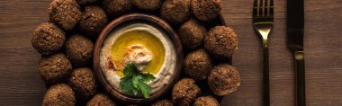 Tahta masadaki çatal bıçak takımının yanında humus kaplı falafel toplarının üst görüntüsü, panoramik çekim.