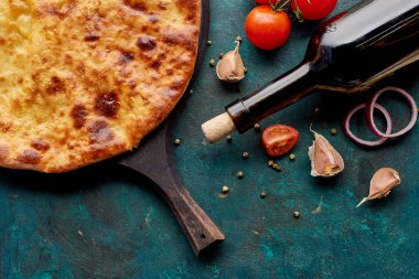 Imereti khachapuri, şarap şişesi ve dokulu yeşil arka planda sebzelerle doğrama tahtasında.