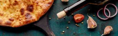Imereti khachapuri with wine bottle and vegetables on textured green background, panoramic shot clipart