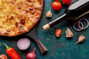 Yeşil arka planda şarap şişesi ve sebzeli imereti khachapuri manzarası.