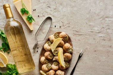 Beyaz şarap şişesinin yanında servis edilen lezzetli salyangozlar ve taştan arkaplanda parmesan.