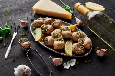 Lezzetli salyangozlar ve limon dilimleri siyah ahşap masa üzerinde baharatlar, parmesan ve beyaz şarap.