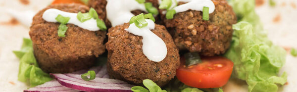close up view of fresh falafel balls on pita with vegetables and sauce, panoramic shot