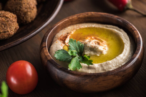 close up view of delicious falafel balls near hummus with parsley on wooden table