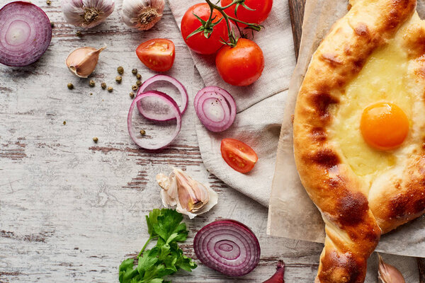 Top view of adjarian khachapuri with vegetables and greens on wooden table