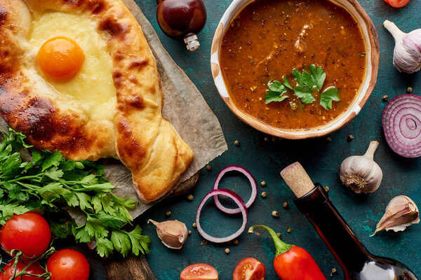 Soup kharcho with cilantro, adjarian khachapuri and wine bottle on textured green background