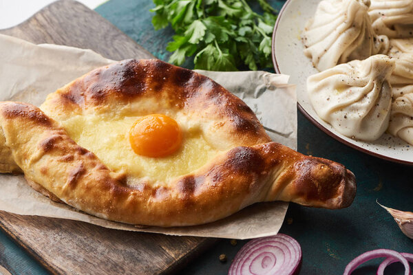 Adjarian khachapuri on cutting board and khinkali with cilantro at background