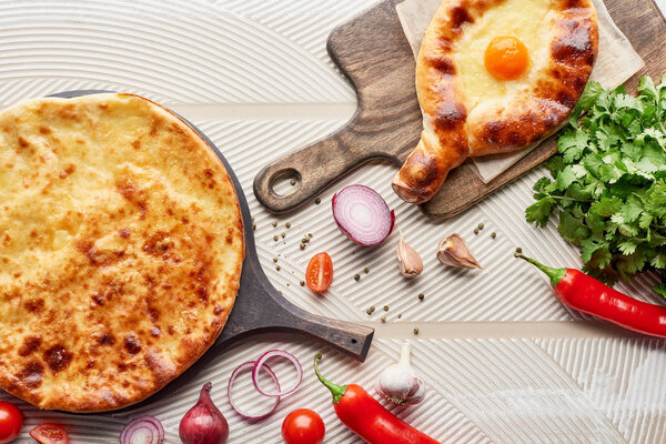Top view of adjarian and imereti khachapuri with vegetables and spices on textured background