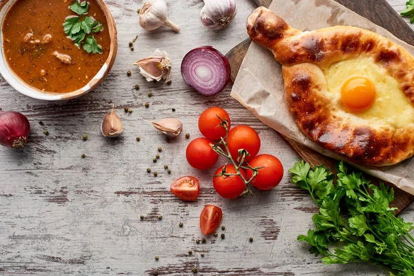 Aadjarian khachapuri and soup kharcho with fresh vegetables on wooden table — Stock Image Aadjarian Khachapuri Soup Kharcho Fresh Vegetables Wooden Table Stock Image