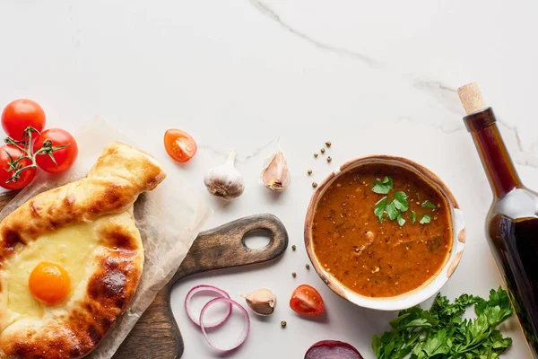 Top view of adjarian khachapuri, soup kharcho, wine bottle and vegetables on marble texture — Stock Image Top View Adjarian Khachapuri Soup Kharcho Wine Bottle Vegetables Marble Royalty Free Stock Photos