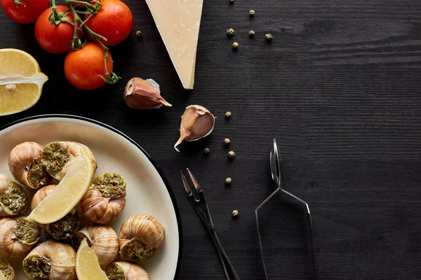 Top view of delicious cooked escargots with lemon slices on black wooden table with ingredients — Stock Image Top View Delicious Cooked Escargots Lemon Slices Black Wooden Table Royalty Free Stock Photos