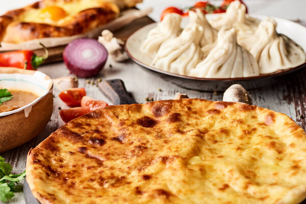 selective focus of Imeretian and Adjarian khachapuri, kharcho and khinkali on wooden table
