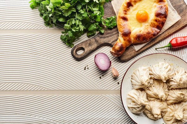 top view of delicious khinkali and adjarian khachapuri near vegetables and spices on beige textured background