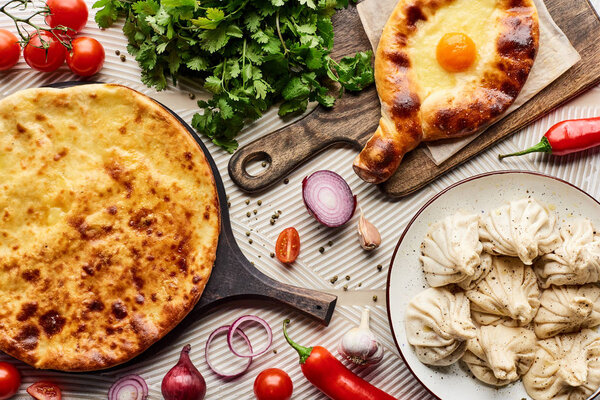 top view of delicious khinkali and khachapuri near vegetables and spices on beige textured background