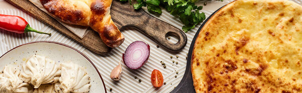 top view of delicious khinkali and adjarian khachapuri near vegetables and spices on beige textured background, panoramic shot