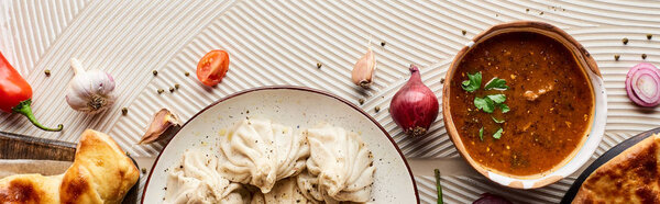 top view of delicious khinkali, kharcho and khachapuri near vegetables and spices on beige textured background, panoramic shot