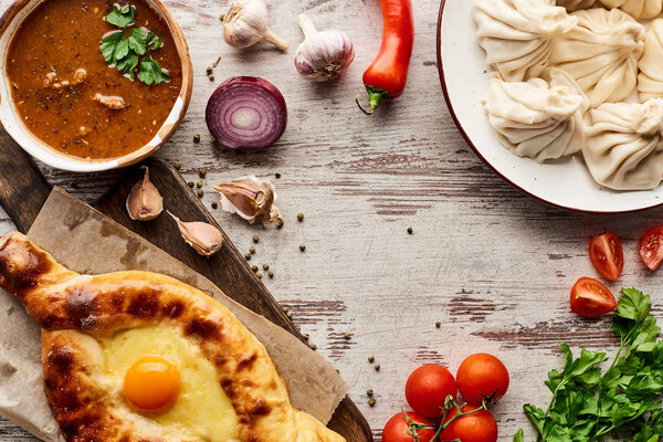 top view of delicious khinkali, adjarian khachapuri, kharcho near vegetables and spices on wooden table