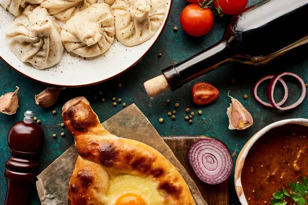 Top view of delicious khinkali, Adjarian khachapuri, kharcho and bottle of wine on green background — Stock Image Top View Delicious Khinkali Adjarian Khachapuri Kharcho Bottle Wine Green Stock Photo