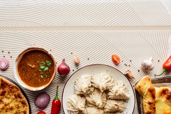 Top view of delicious khinkali, kharcho and khachapuri near vegetables and spices on beige textured background — Stock Image Top View Delicious Khinkali Kharcho Khachapuri Vegetables Spices Beige Textured Stock Picture