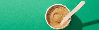 top view of depilation wax in cup with stick on green background, panoramic shot clipart