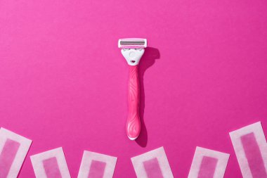 Kadın traş makinesinin üst görüntüsü ve pembe arka planda tüy dökücü balmumu çizgileri