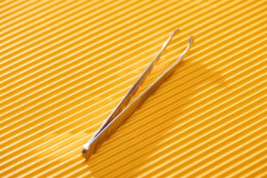 stainless steel tweezers on yellow textured background clipart